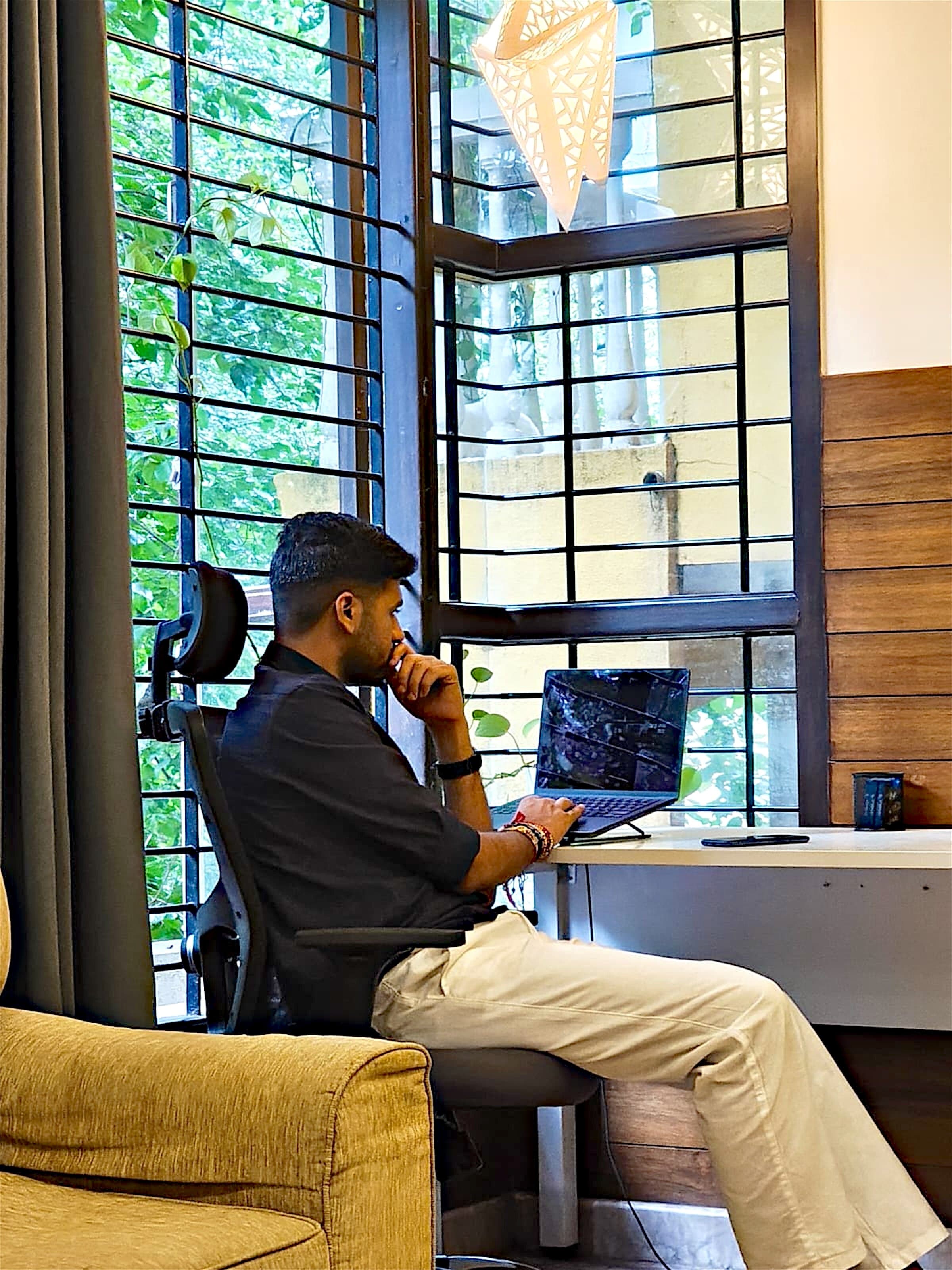 Abhinav Verma at his desk by a window, hand on chin, thinking over something on his laptop
